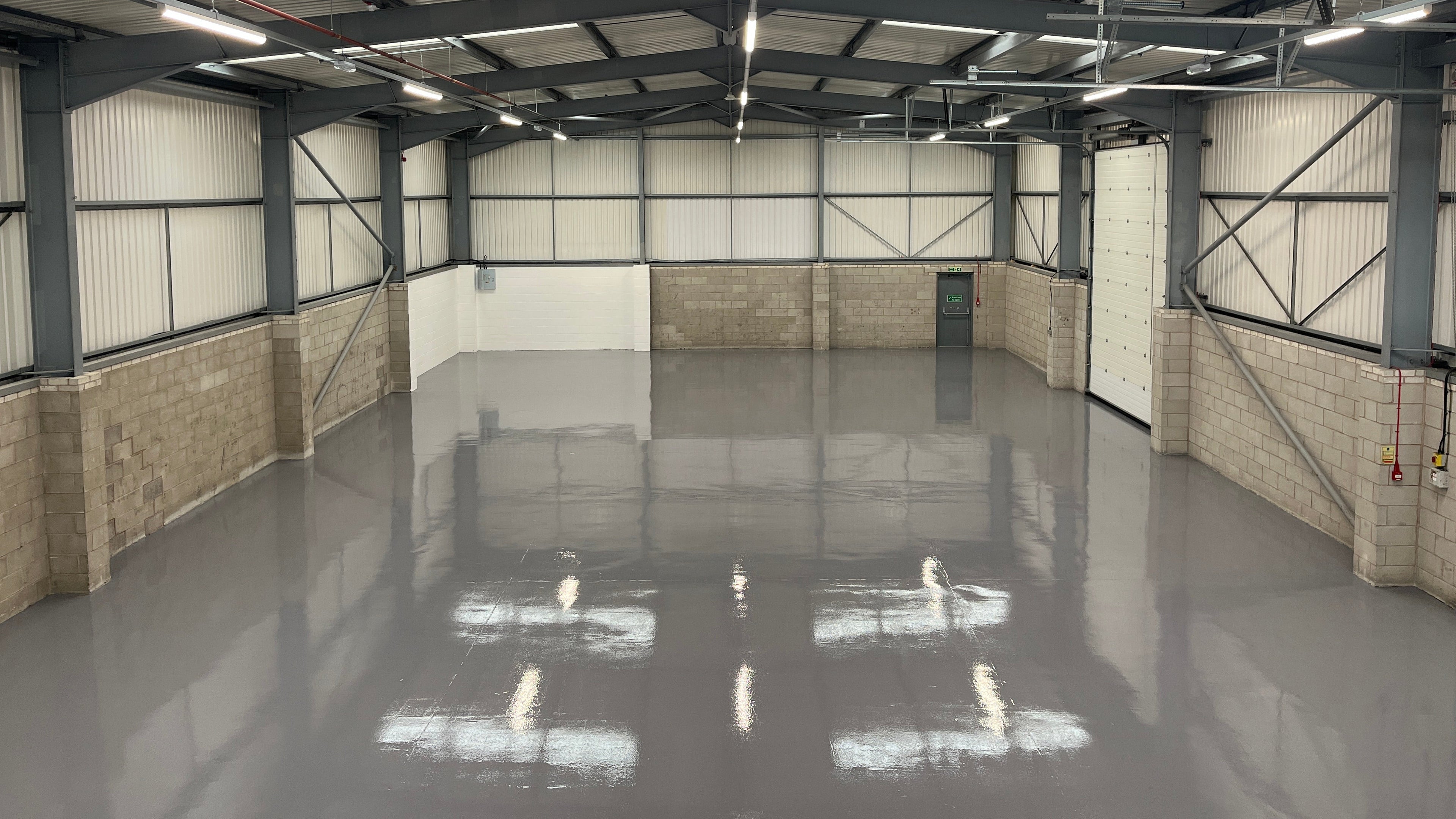 Grey epoxy floor coating in a large industrial warehouse with block walls, steel beams and overhead lighting.